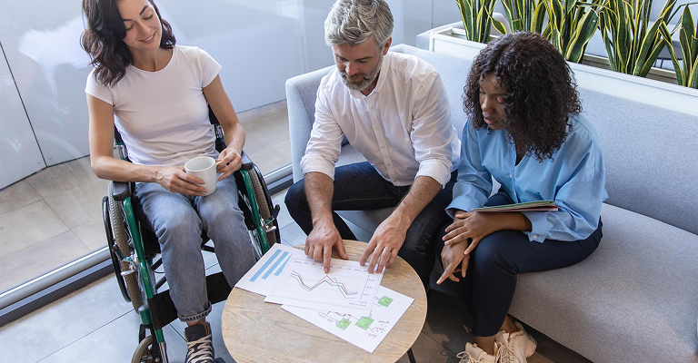 a group of people sitting on the couch and looking at the graph, a lady sits in a wheelchair holding a cup
